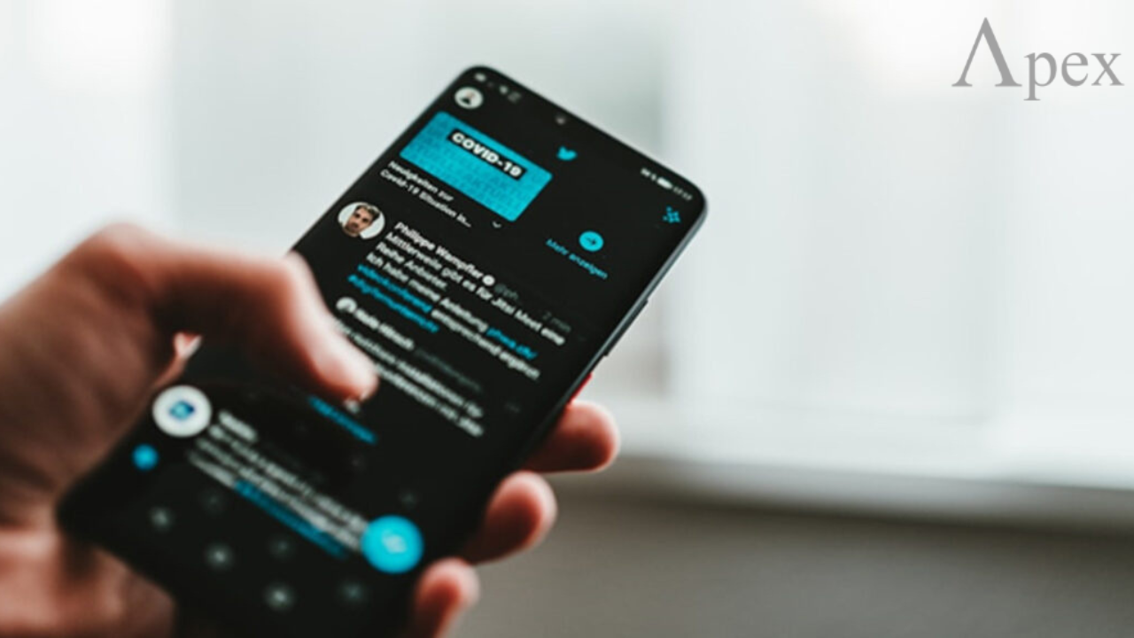 Hand holding a phone showing a public Twitter feed in the app.